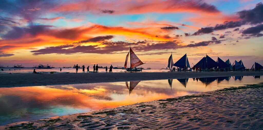 The image shows a vibrant sunset over White Beach in Boracay Island